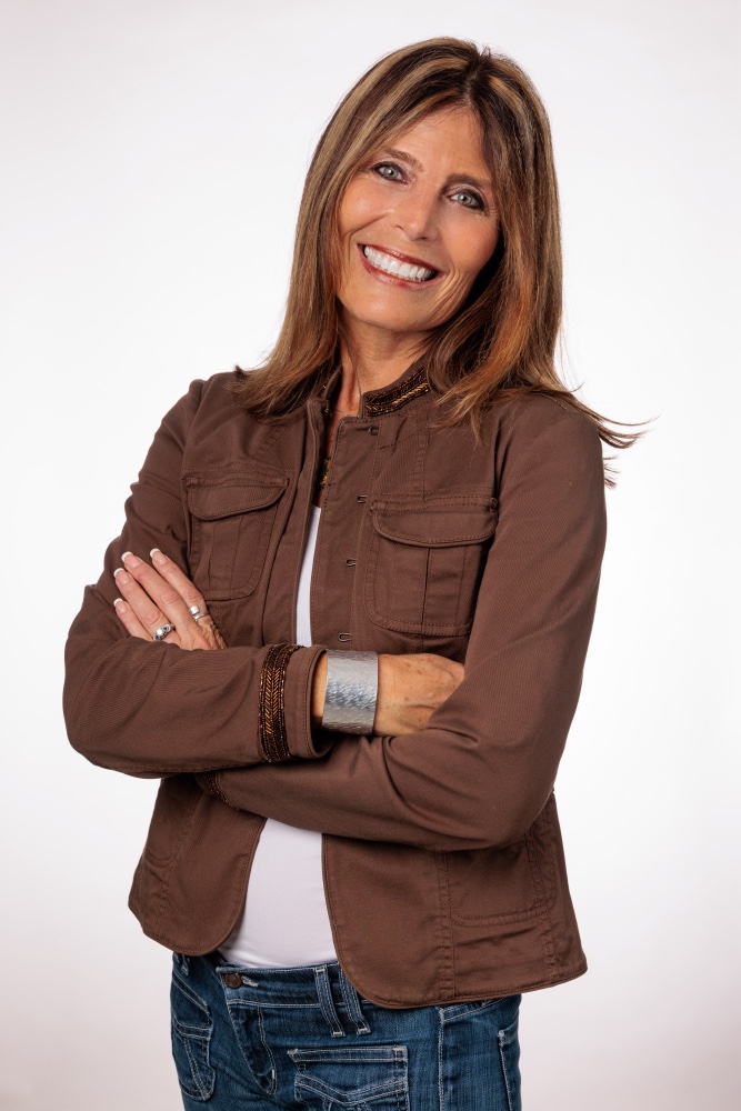 Carolyn Gomez studio headshot in a brown jacket, arms crossed — the confident alternate, matching the cover composite